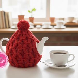 Pode incluir: Uma chaleira de cerâmica branca com uma capa de malha vermelha e um pompom a condizer. Uma chávena branca com café está num pires ao lado da chaleira. O texto "Shop: TheSweetest CrochetPT" está num autocolante rosa.