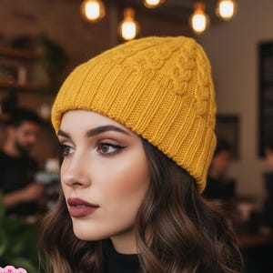 May include: Mustard yellow knit beanie with a cable knit design. The hat is worn by a person wearing a black turtleneck. The background includes a cafe setting with warm lighting and the text "Shop: TheSweetest CrochetPT".