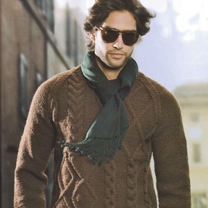 Puede incluir: Un suéter de punto de cable marrón con una bufanda verde oscuro. El hombre lleva gafas de sol.