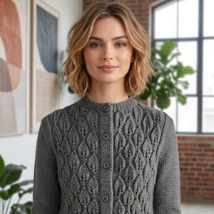 May include: A charcoal gray knit cardigan featuring a repeating leaf-like textured pattern, a round neckline, and a front button closure. The garment has three-quarter length sleeves with ribbed cuffs and a pink circular logo reading Shop: TheSweetestCrochetPT.