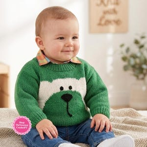 Könnte beinhalten: Ein grüner, langärmeliger Strickpullover mit einem weißen Bärengesicht-Motiv, schwarzen Augen und einer schwarzen Nase, getragen über einem karierten Hemd mit Kragen und blauen Jeans, kombiniert mit weißen Schuhen. Der Pullover hat gerippte Bündchen.