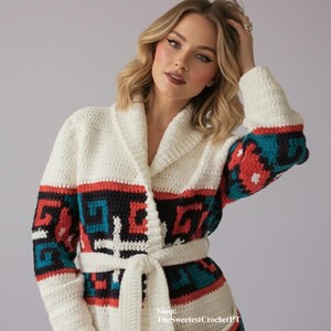 May include: Cream-colored crochet robe with a shawl collar and a matching belt. The sleeves and pockets feature a geometric pattern in teal, red, and black. The robe is a cozy, handmade garment.