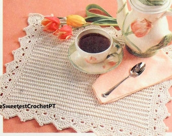 Op de afbeelding: Een vierkante, gebroken witte gehaakte placemat met een decoratieve schulprand. De placemat heeft een gestructureerd ribbelpatroon en bevat de tekst TheSweetestCrochetPT in het zwart gedrukt in de linkerbenedenhoek van de stof.