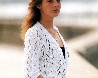 May include: A white, short-sleeved, open-front cardigan featuring an intricate, repeating chevron lace pattern with a scalloped edge along the hem and sleeves. The garment is knitted with a lightweight yarn and includes the text TheSweetestCrochetPT.