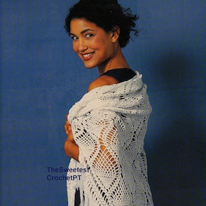 Può includere: Uno scialle bianco all'uncinetto con un delicato motivo a pizzo e frange. Lo scialle è drappeggiato sulla spalla di una persona con i capelli ricci.