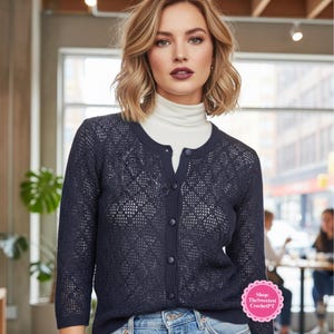 Op de afbeelding: Marineblau vest met open weefsel en knoopsluiting. Het vest wordt gecombineerd met een witte coltrui en lichtblauwe jeans. De afbeelding bevat een shoplogo in de rechter benedenhoek.