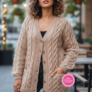 May include: A beige cable-knit cardigan with a V-neck, button closure, and two front pockets. The long-sleeved sweater features a textured cable design and is worn over a black top and dark jeans. The image includes the text "Shop TheSweetest CrochetPT".