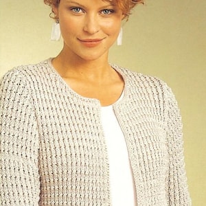 May include: A cream-coloured, open-front cardigan with a textured, vertical knit pattern. The long-sleeved sweater has a round neckline and is worn over a white top. The text "Shop: TheSweetestCrochetPT" is visible.