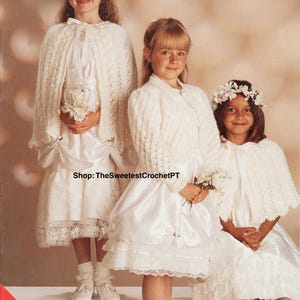 Könnte beinhalten: Drei junge Mädchen in weißen Kleidern und gehäkelten Umhängen. Die Kleider haben Spitzensaum und Satinstoff. Die Mädchen tragen weiße Schuhe und Socken. Ein Mädchen hat einen Blumenkranz. Der Text "Shop: TheSweetestCrochetPT" ist enthalten.
