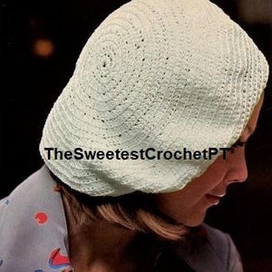 May include: A light cream-coloured crocheted beret featuring a circular pattern with small, evenly spaced perforations throughout the fabric. The text TheSweetestCrochetPT is printed across the centre of the hat in a dark, bold font.