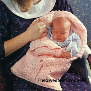 以下が含まれることがあります： ボタン留めのピンクの編みぐるみベビーブランケット。ブランケットは寝ている赤ちゃんの周りに巻かれています。