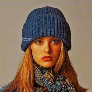 Könnte beinhalten: Eine blaue Häkelmütze mit gerippter Struktur. Die Mütze wird von einer Person mit langen, hellbraunen Haaren getragen. Die Person trägt einen blau-grünen Häkelschal.