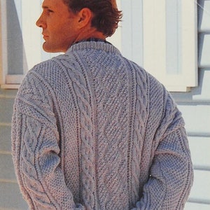 May include: A gray cable knit sweater with a crew neck. The sweater has a textured pattern with a cable knit design.