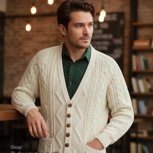 Puede incluir: Cárdigan de punto de color crema con cuello en V, botones de madera y dos bolsillos delanteros. El suéter tiene un diseño texturizado y se usa sobre una camisa verde abotonada y jeans azules. Un estilo clásico.