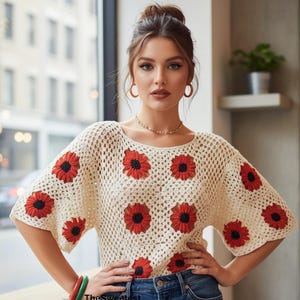 Könnte beinhalten: Ein cremefarbenes Häkeloberteil mit einem sich wiederholenden Muster aus roten und schwarzen Blumenmotiven, kurzen Ärmeln und einem Rundhalsausschnitt, kombiniert mit einer blauen Jeans. Der Text TheSweetestCrochetPT ist unten vorne sichtbar.