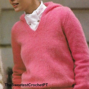 Könnte beinhalten: Ein rosa flauschiger Pullover mit V-Ausschnitt und einem Kordelzug am Saum. Der Pullover wird über einem weißen Hemd mit Kragen getragen.