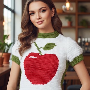 Può includere: Top all'uncinetto bianco con un grande design a mela rossa, rifiniture verdi su colletto e maniche. Il testo "Shop: TheSweetestCrochetPT" è visibile. Il top è a maniche corte e girocollo.