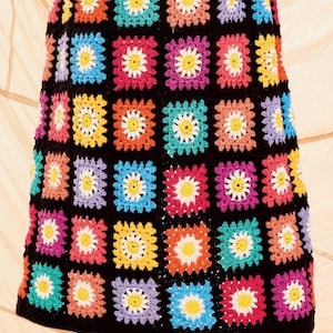 Pu&ograve; includere: Una gonna a uncinetto colorata con sfondo nero e un motivo a margherita. La gonna &egrave; composta da pi&ugrave; quadrati di diversi colori, tra cui rosa, blu, giallo, verde e viola.