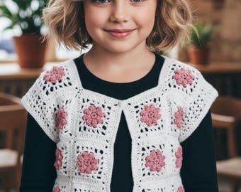 Puede incluir: Un chaleco de ganchillo blanco con un diseño de cuadrados y motivos florales rosas. La prenda se lleva sobre una camiseta negra de manga larga. El texto "Shop: TheSweetestCrochetPT" es visible en la esquina inferior izquierda.