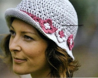 May include: A gray crochet hat with a pink and white flower trim. The hat has a wide brim and is worn by a person with brown hair.