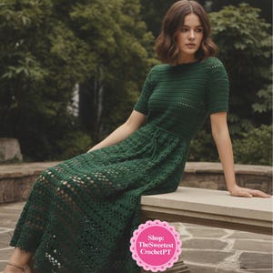 Puede incluir: Vestido de ganchillo verde oscuro con mangas cortas y falda fluida. El vestido presenta un patrón calado detallado y un corpiño ajustado. La modelo está sentada en un banco de piedra. El vestido es de TheSweetestCrochetPT.