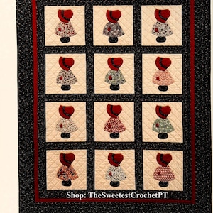 Könnte beinhalten: Ein Quiltblock mit schwarzem Hintergrund und rotem Rand. Der Block zeigt 12 applizierte Figuren von Frauen in roten Hüten und Kleidern mit Blumenmustern. Der Text "Shop: TheSweetestCrochetPT" befindet sich am unteren Rand des Blocks.