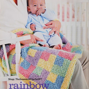 Könnte beinhalten: Eine bunte gehäkelte Babydecke mit einem Regenbogenmuster. Die Decke ist aus verschiedenen Farbtönen von Rosa, Blau, Grün und Gelb gefertigt. Die Decke liegt auf einem Schaukelstuhl, auf dem ein Baby sitzt. Der Text "Shop: TheSweetestCrochetPT" und "rainbow blanket" ist unten im Bild sichtbar.