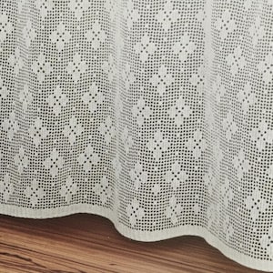 Puede incluir: Una cortina de ganchillo blanca con un patrón floral geométrico repetitivo en toda la tela. El tejido tiene una estructura de rejilla abierta y delicada con pliegues suaves a lo largo del borde inferior. Un pequeño logotipo circular rosa incluye el texto Shop: TheSweetestCrochetPT.