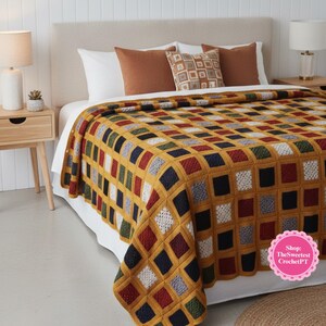 Könnte beinhalten: Handgefertigte Häkeldecke mit einem geometrischen Muster aus Quadraten in verschiedenen Farben, darunter Senfgelb, Rot, Marineblau und Weiß. Die Decke liegt auf einem Bett mit Kissen und schafft eine gemütliche Atmosphäre. Ein dekorativer Artikel.