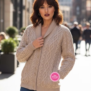 Puede incluir: Cárdigan beige de punto trenzado con cuello chal y cierre de botones. El suéter tiene un patrón texturizado y mangas largas. La modelo lleva vaqueros azules. Incluye el texto "Shop The Sweetest CrochetPT".