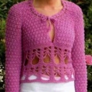 May include: A pink crocheted cardigan with a lace pattern and a tie at the neckline. The cardigan is worn over a white skirt with a floral design.