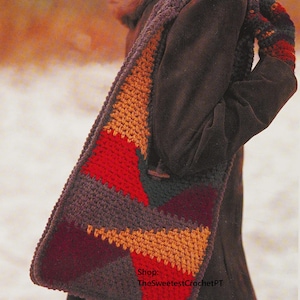 May include: A handcrafted crochet scarf featuring a geometric design in red, orange, burgundy, and grey. The scarf is worn over a dark brown coat. The text "Shop: TheSweetestCrochetPT" is visible.