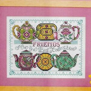 以下が含まれることがあります： 5つのカラフルなティーポットと「Tea Friends Are the Best Collectibles」というテキストのクロスステッチ刺繍。