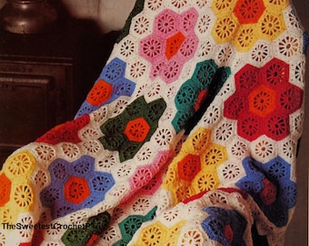 May include: A colorful crochet blanket with a geometric pattern of hexagons and flowers in shades of red, orange, yellow, green, blue, and pink. The blanket is draped over a chair.