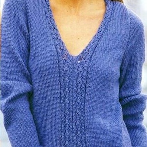 May include: A periwinkle blue knitted jumper with a V-neck and long sleeves. The jumper features a central cable knit design and a decorative trim along the neckline. The text "Shop: TheSweetestCrochetPT" is visible.