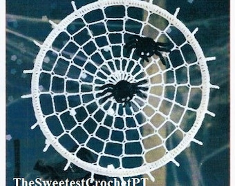 Può includere: Una ragnatela circolare lavorata all'uncinetto in bianco con due ragni neri dagli occhi bianchi fissati al centro e nella parte superiore destra. La ragnatela presenta un motivo a raggiera con piccole punte sul bordo. Il testo TheSweetestCrochetPT è visibile.