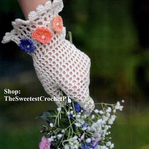 Könnte beinhalten: Ein weißer Häkelhandschuh mit einem gewellten Rand und drei gehäkelten Blumen in Blau-, Orange- und Rosatönen. Der Handschuh hält einen Strauß weißer, rosa und blauer Blumen.