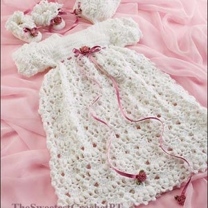 May include: A white crocheted baby dress with a pink satin ribbon and a matching crocheted hat. The dress has a delicate lace pattern and is perfect for a special occasion.