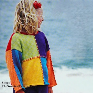 May include: A young person wearing a colorful crocheted sweater with a patchwork design. The sweater is made of different colored squares of yarn, including orange, yellow, green, blue, and purple. The person is standing on a beach with the ocean in the background. The text "Shop: TheSweetestCrochetPT" is visible in the bottom left corner of the image.