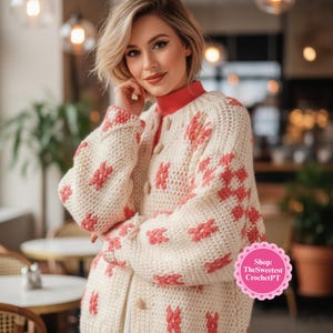 May include: Cream-colored, button-down cardigan with a red geometric pattern. The chunky knit sweater has a round neckline and long sleeves. The cardigan is part of a collection of handmade crochet items.