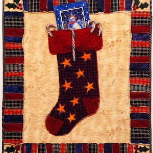 May include: A quilted Christmas stocking with a dark purple body and orange stars. The stocking is filled with a card featuring a snowman and candy canes. The border is made of plaid fabric in red, blue, and black.