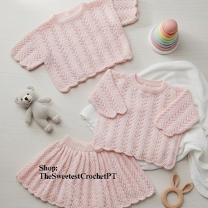 May include: A light pink knitted baby outfit set, including a short-sleeved top, a long-sleeved top, and a skirt. The set is displayed with a small stuffed bear, a wooden bunny teether, and a colorful stacking toy.