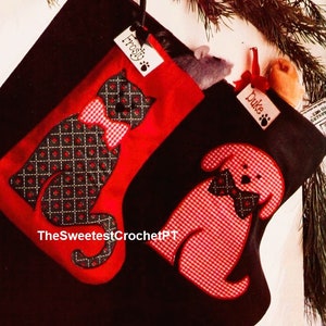 May include: Two red and black Christmas stockings with a cat and dog design. The cat stocking has a black cat with a red bow tie and the text "Frosty" on a tag. The dog stocking has a red dog with a black bow tie and the text "Duke" on a tag.