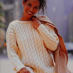 May include: A cream-colored cable knit sweater with a relaxed fit. The sweater has a round neckline and long sleeves.