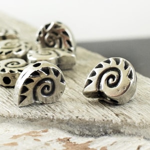 May include: Silver-toned metal beads with a spiral design. The beads are shaped like a seashell and have a textured surface.