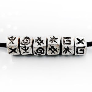 Può includere: Una collana d'argento con un cordoncino in pelle nera e perline d'argento. Ogni perlina ha un simbolo diverso inciso.