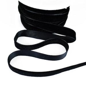 May include: Black velvet ribbon with a soft, plush texture. The ribbon is folded and rolled up, showing the width and the smooth, even surface.