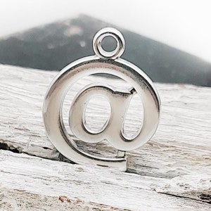 Könnte beinhalten: Silberner Anhänger in Form eines @-Symbols, ein häufig verwendetes Symbol in E-Mail-Adressen.