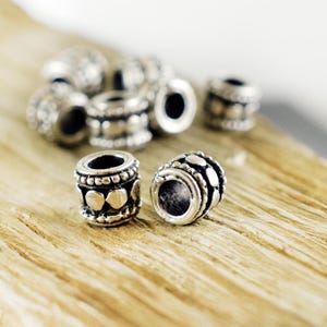May include: Silver metal beads with a decorative pattern. The beads are round and have a smooth surface.