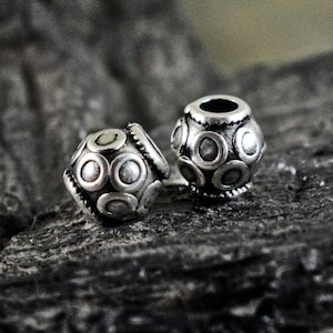 May include: Two silver beads with a circular pattern. The beads are round and have a textured surface.